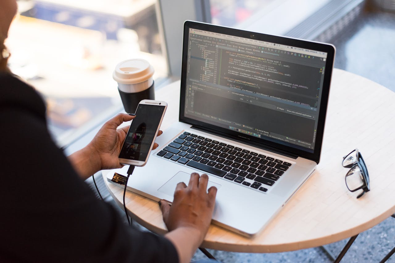 why-choose-us Developer working remotely, coding on a laptop with phone in hand, showcasing modern work culture.
